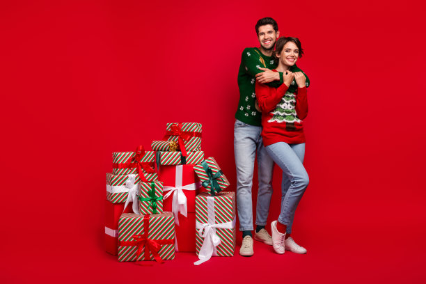 两位宁静理想的伴侣在红色背景上堆叠在一起，准备新年礼物派对的全身照片。图片下载