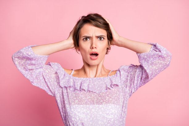 惊慌失措的女性用双手捂住头部的照片肖像，背景为柔和的粉色。图片下载