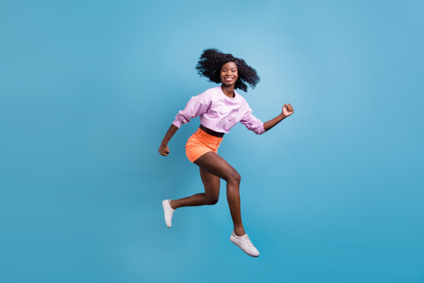 年轻快乐美丽的微笑非洲女孩在蓝色背景上奔跑的全身侧面照片图片下载