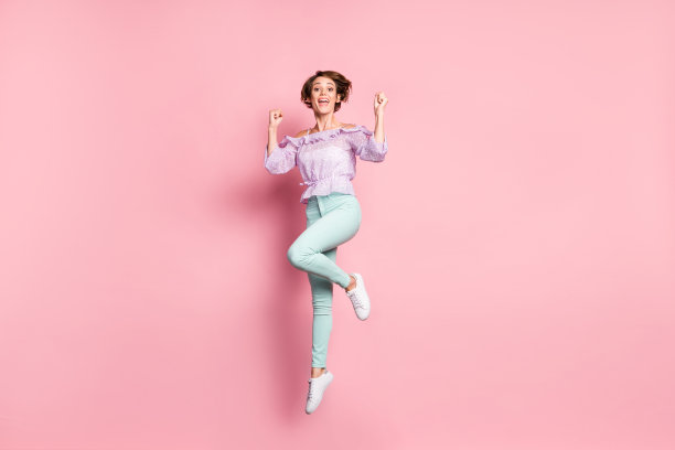 年轻可爱快乐兴奋的女孩在粉色背景上跳跃庆祝胜利成功的全身照片图片下载