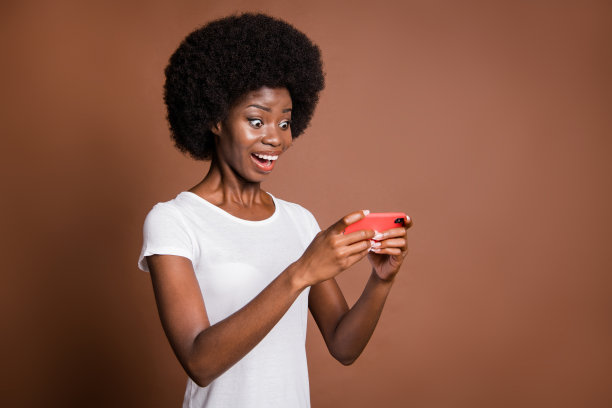 模特在棕色背景下兴奋地微笑着玩手机游戏的照片肖像图片下载