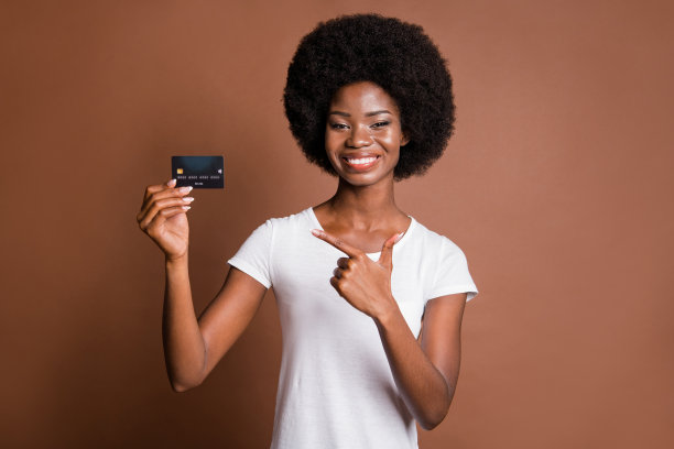 穿着休闲服的女性在棕色背景前微笑，手指着信用卡拍摄的肖像照片图片下载