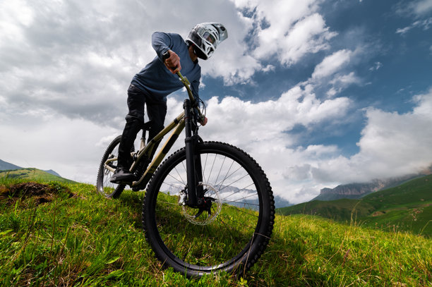 山地自行车手在草坡上骑行。越野山地车。山地车与山景相映。图片下载