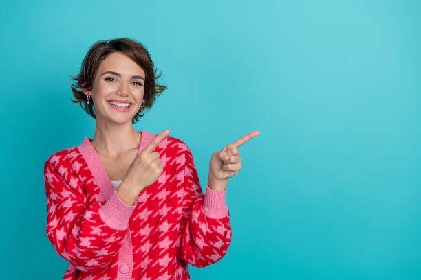 漂亮年轻女孩的照片肖像，指向空白处，穿着时尚的红色服装，背景为水绿色。图片下载