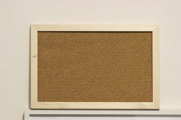 一个简单的木框软木公告板，靠在中性色的墙壁上。非常适合在家中或办公室整理便条、提醒和照片。图片下载