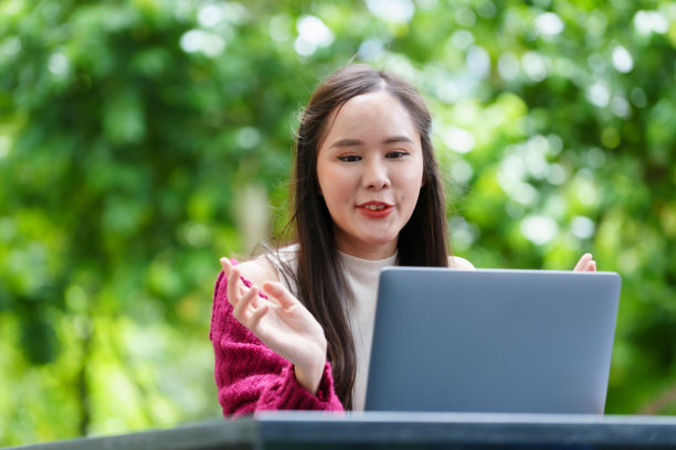 一位女性在公园的假期中愉快地坐着，使用笔记本电脑并听着音乐（照片）图片下载