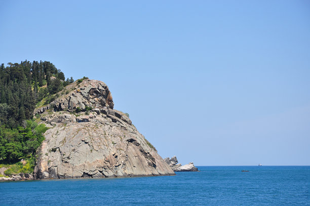 岩石海岸悬崖形似猫头鹰的头部，顶部有森林，下面是蓝色海洋，清澈的天空下，独特的自然岩石形成和风景如画的景观，适合旅行、自然和野生动物项目。图片下载