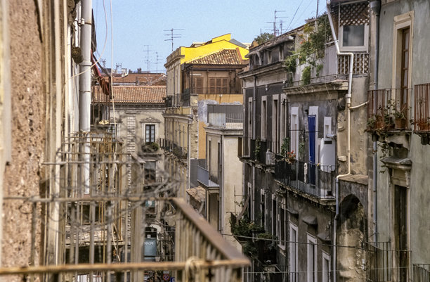 西西里岛卡塔尼亚老城区的后院历史彩色照片，展示了阳台、窗户和剥落的住宅外立面。图片下载