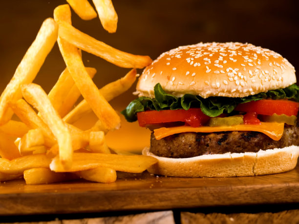 一份熟透的汉堡，配有牛肉饼、西红柿、生菜和奶酪。旁边是一份奶酪汉堡，上面洒着薯条。特写广告照片。图片下载