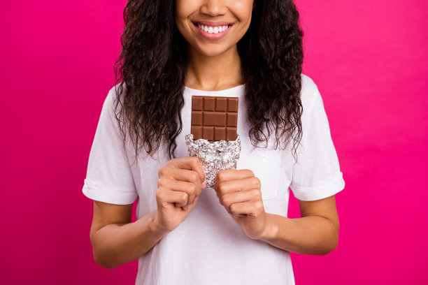 有趣的棕发年轻女士穿着白色T恤，手持巧克力，背景为粉色，照片经过裁剪。图片下载