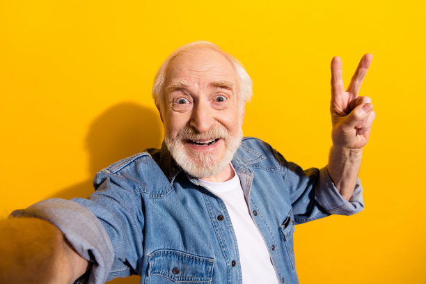 爷爷在鲜艳的黄色背景下微笑着做出V字手势自拍的照片肖像图片下载