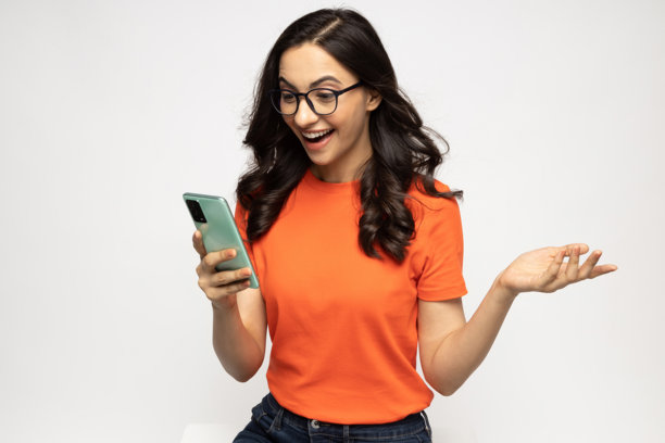 年轻女性穿着现代服装使用手机的照片，背景为白色。图片下载