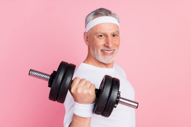老年男子在粉色背景下保持强壮的手臂，手握重哑铃的肖像照片图片下载