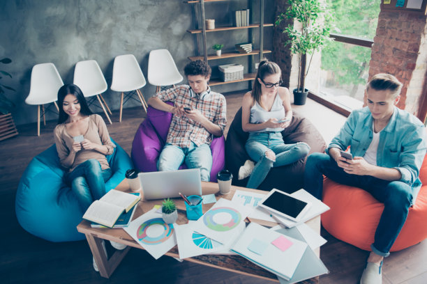 一群人坐在豆袋椅上，使用电话，准备在室内办公室进行测试的全景照片图片下载