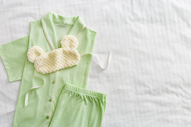 俯视折叠的淡绿色女性睡衣和毛绒睡眠眼罩，放在白色床上。简约的平铺舒适睡衣，适合睡觉和放松。时尚睡衣的美学生活方式照片。图片下载