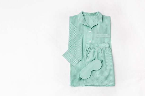 俯视折叠的条纹绿色女式睡衣和白色床上的缎面睡眠眼罩。简约的平铺舒适睡衣，适合睡眠和放松。时尚睡衣的美学生活方式照片。图片下载