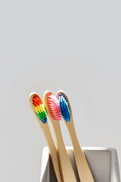 环保竹牙刷，彩色刷毛，放置在方形灰色混凝土牙刷架中，阳光照射下伴有窗户投射的阴影。可持续生活理念，极简风格美学照片。图片下载