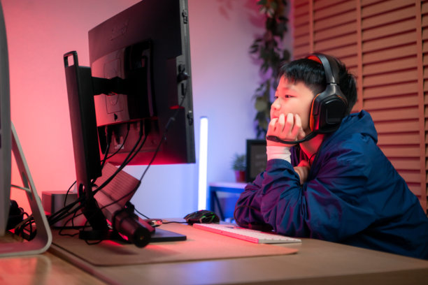 一个戴着耳机的男孩在色彩缤纷的游戏设置中使用台式电脑玩游戏图片下载