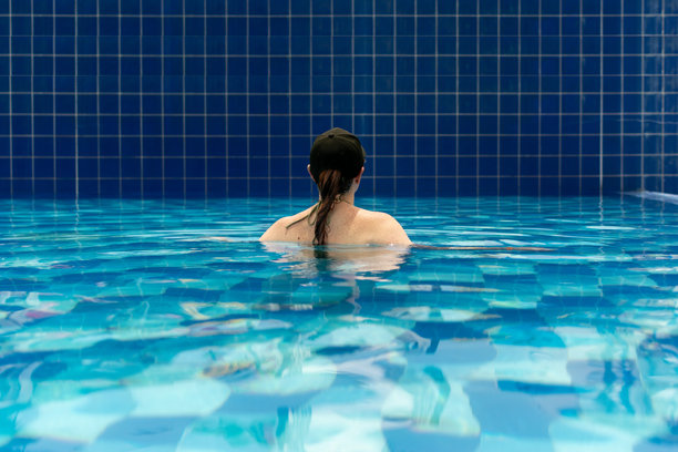 一位戴着黑色棒球帽和太阳镜的宁静女性在碧绿色的泳池中放松。这张图片捕捉了独自旅行中的宁静时刻，反映出一种平和而宁静的度假生活方式。图片下载