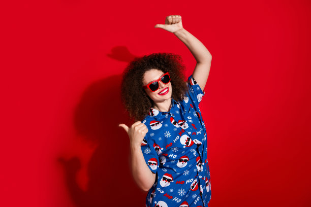 漂亮年轻女孩的照片肖像，手指指向空白处，穿着时尚的蓝色圣诞图案服装，背景为红色。图片下载