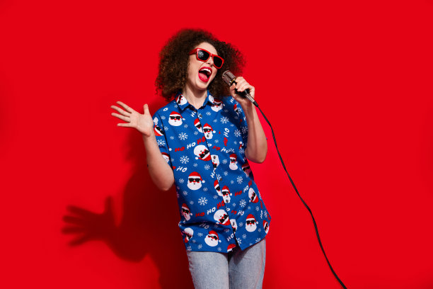 漂亮年轻女孩的照片肖像，穿着时尚的蓝色印花圣诞服装，手持麦克风跳舞唱歌，背景为红色。图片下载