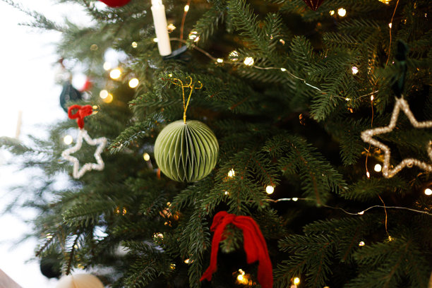 时尚的圣诞纸饰品，复古的星星和蜡烛在树枝上特写，现代装饰的圣诞树在客厅中闪烁着金色灯光。圣诞快乐，节日快乐！图片下载