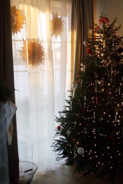 时尚的圣诞树装饰着红色蝴蝶结、饰品、复古星星、蜡烛和金色灯光，营造出温馨的客厅氛围，魔幻的夜晚。圣诞快乐，节日快乐！图片下载