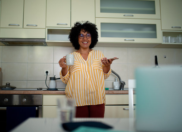 女人在厨房微笑，手里拿着咖啡和手机 - 股票照片图片下载