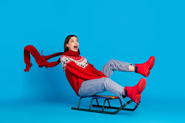 年轻女孩的全身侧面照片，开心、积极、微笑，兴奋地在冬天的蓝色背景下快速滑雪，围着围巾。图片下载