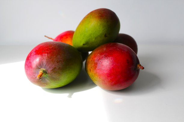 美丽而独特的构图，展示美味的成熟热带芒果。健康有机食品概念。照片背景为白色，带有明显的阴影，并留有文字空间。图片下载