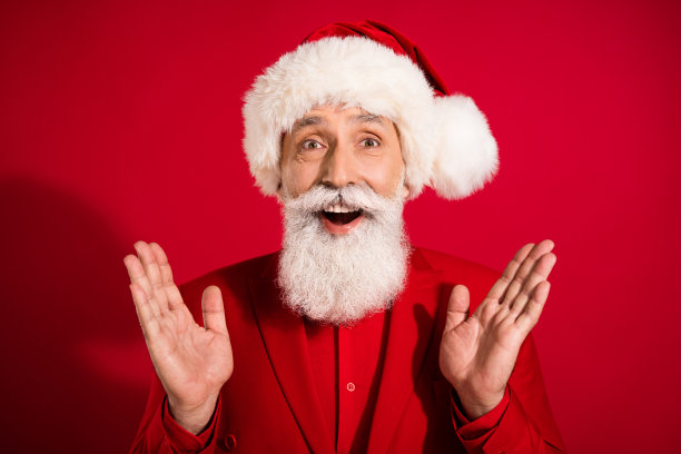 搞笑的灰发老人在红色背景下穿着圣诞帽和红色西装的照片图片下载