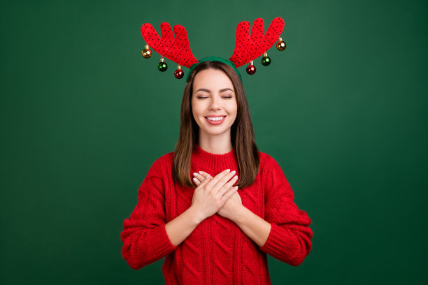 年轻女孩开心地微笑，双手放在胸前，满怀感激，头戴发带，背景为绿色。图片下载