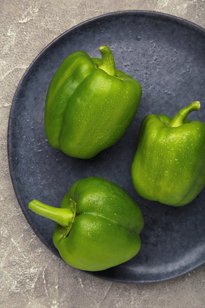 深色盘子上的绿色甜椒，背景为灰色。竖版照片图片下载