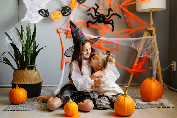 一张感人的抓拍照片，展示了两个年轻姐妹穿着万圣节服装，在装饰一新的房间里相拥微笑。图片下载