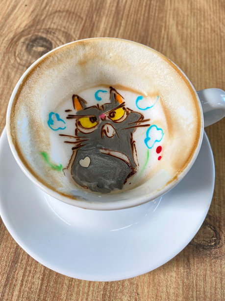 一张带有奇思妙想猫咪插画和多彩点缀的艺术咖啡杯，展示了在舒适咖啡馆环境中富有创意的拿铁拉花艺术，非常适合美食与饮品爱好者。图片下载