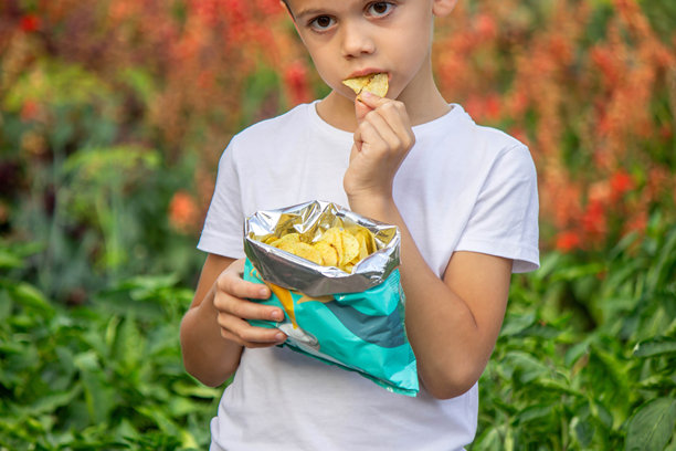 男孩从包装袋里吃薯片。不健康食品概念图片下载