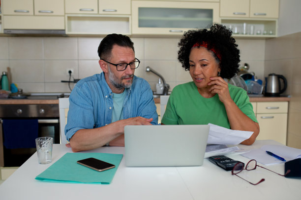 成熟夫妇在家中管理财务，使用笔记本电脑和文件 - 库存照片图片下载