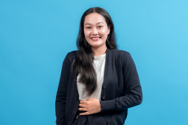 一位有着黑色长发的快乐女性，穿着开衫，面带微笑，在蓝色背景前摆姿势。这张照片捕捉了幸福、自信和休闲风格，背景充满活力。图片下载