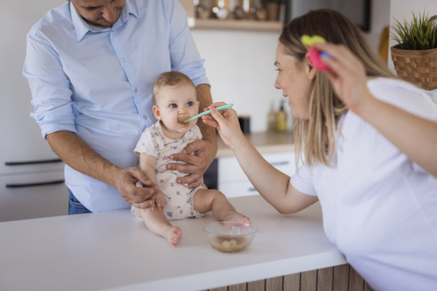 父母在厨房喂婴儿辅食：充满爱的家庭用餐时光图片下载