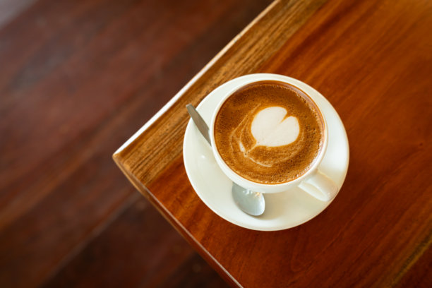 咖啡店早餐，热咖啡拿铁，杯子上的拉花奶泡，放在木桌上，俯视角度。适合工作场景，复古风格。图片下载