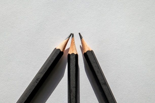三支黑色铅笔在白纸上对准中心点的极简主义照片。锐利的阴影和干净的构图图片下载