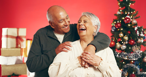 Hug, laugh and senior couple with Christmas in studio with love, festive and marriage tradition. Happy, retirement and elderly man embracing woman by xmas tree for celebration on red background.图片下载