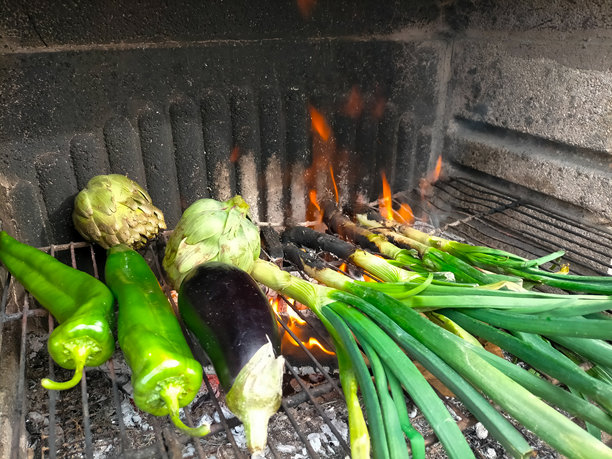 男人在烤架上烤肉、洋葱、蔬菜，伴随着火星、烟雾和火焰，特写他烹饪的手。图片下载