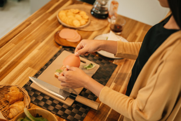 close-up of a woman's hands layering fresh deli meat on bread while making a homemade sandwich in a cozy kitchen图片下载
