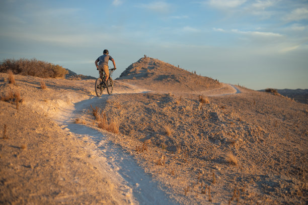 夕阳下，山地车手在沙漠赛道上骑行图片下载