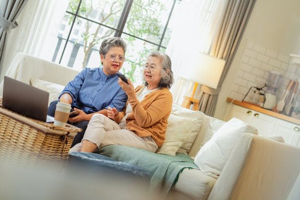 亚洲老年女性在家舒适的沙发上与亲密的朋友一起浏览珍贵的照片回忆，分享感人的故事，巩固一生情谊，享受怀旧时光。图片下载