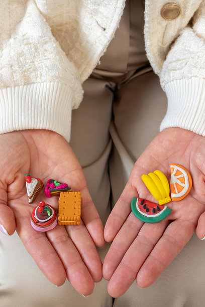 女性手掌特写，上面有不健康和健康食物的微缩模型。蛋糕、饼干、糖果、水果的小模型。健康生活方式和均衡饮食的概念。竖幅照片。图片下载