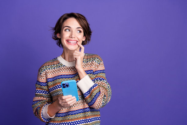 照片，一位身穿时髦服装、手持小工具、眼神空洞、孤立在紫色背景前的快乐可爱狡猾的女人。图片下载