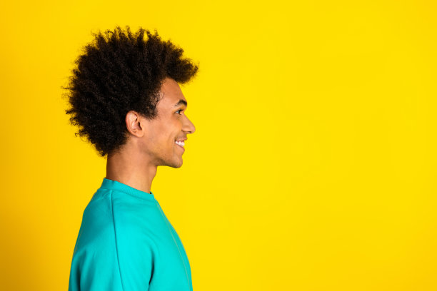 照片：一位穿着青绿色套头衫、留着非洲式卷发的快乐青年，背景是鲜艳的黄色。图片下载