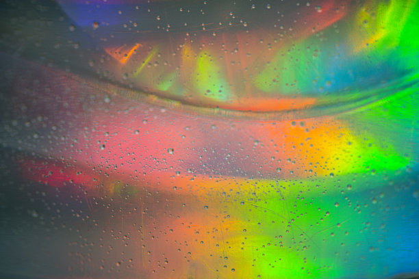 抽象特写照片，展示绿色、橙色和蓝色调的彩色光线反射，带有大量小水滴图片下载